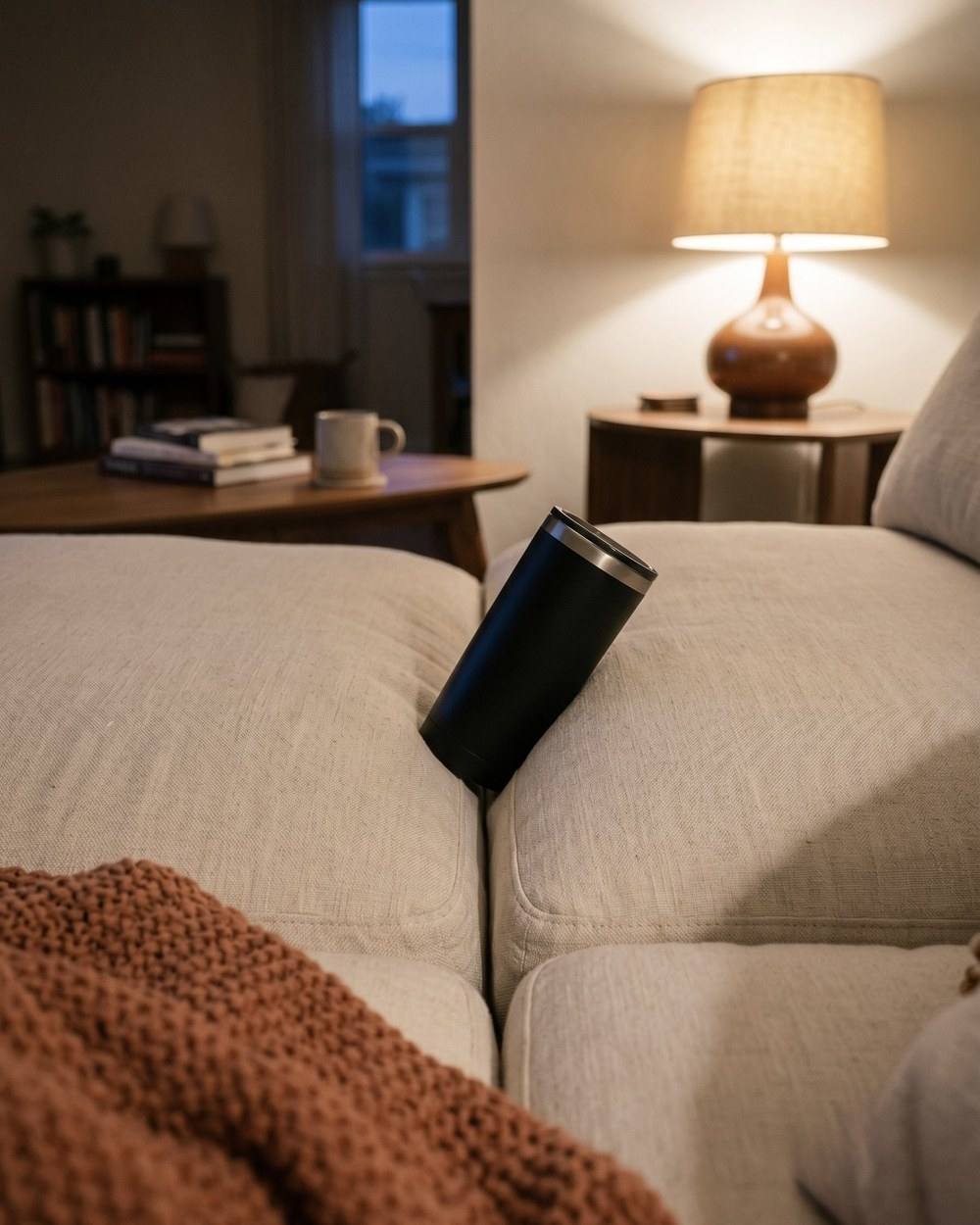 A tumbler wedged between two couch cushions, tilted.