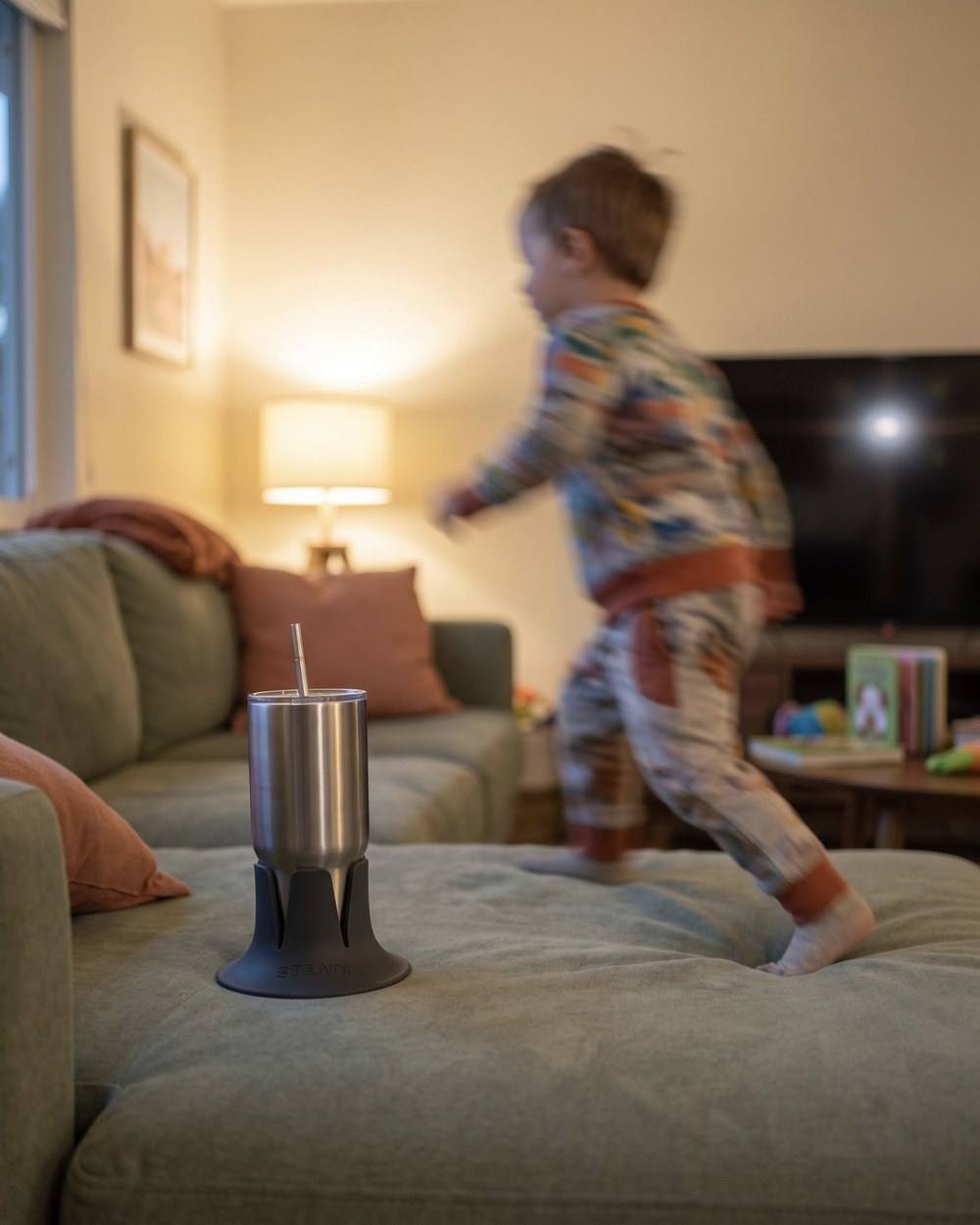 A toddler running across the couch cushion while a tumbler stays level in a charcoal base on the same cushion.
