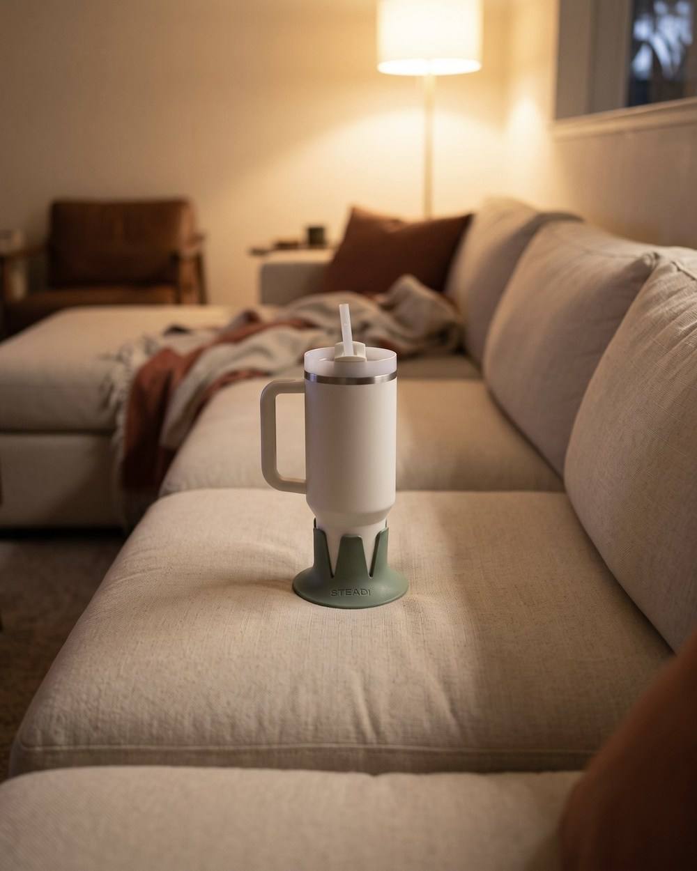 A 40 oz tumbler seated in a sage drink base on the middle cushion of a sectional, floor lamp behind.